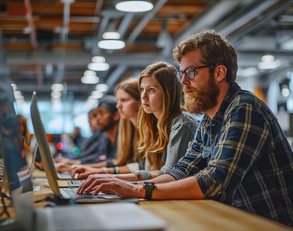 Young professionals working intently on laptops in a modern, open-plan office setting, showcasing teamwork and focus